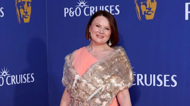 Monica Dolan on red carpet in peach dress with fur shoulder cover