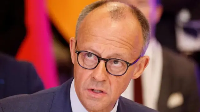 Close-up shot of German Chancellor Friedrich Merz with a colourful oink and orange blurred background