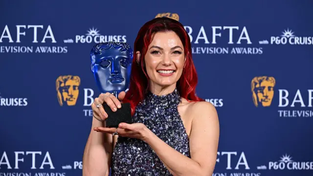 Dianne Buswell holds up the blue Bafta award as she smiles to the camera