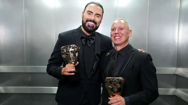 Rylan Clark and Rob Rinder pose inside a lift with their Bafta awards