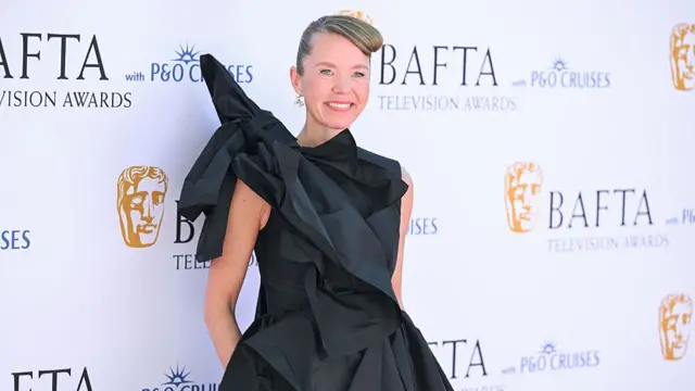 Anna Maxwell Martin  with her hair up wears a black ball gown with massive bow on her right shoulder