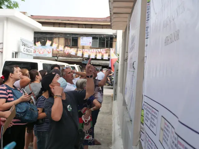 People at a polling station in the Philippine look up at candidate lists.