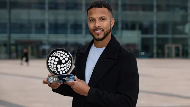 Joe Thompson, pictured in 2019, with the EFL's Sir Tom Finney Award for outstanding contribution to the game. He is wearing a black coat over a white t-shirt as he smiles for the camera while holding a round EFL-branded trophy