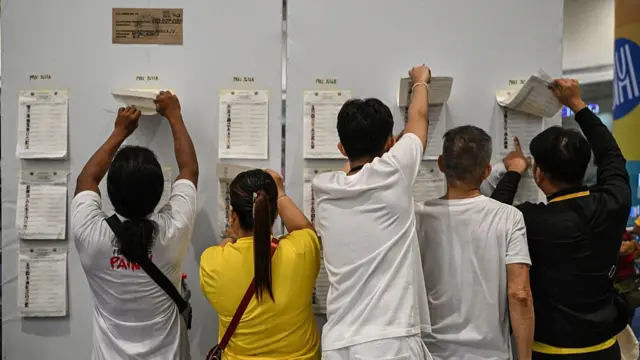 Five people checking registration lists on a wall at a polling station