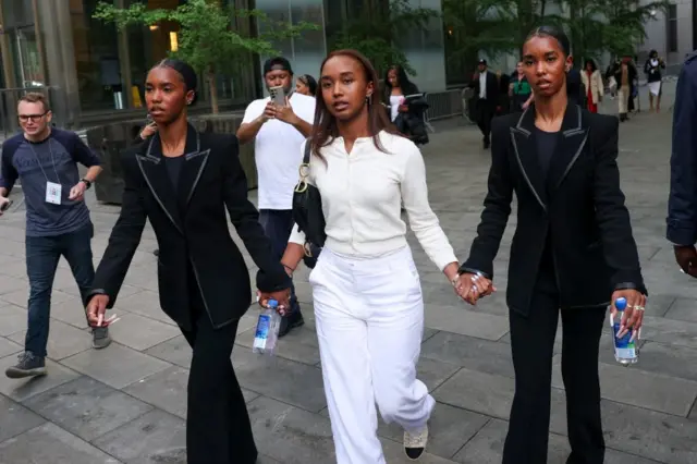Three women holding hands walk outside court