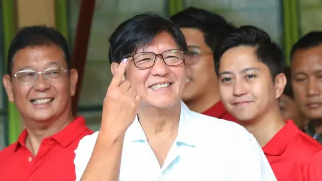 Bongbong Marcos smiles as he raises his index finger. Behind him is his son Sandro.