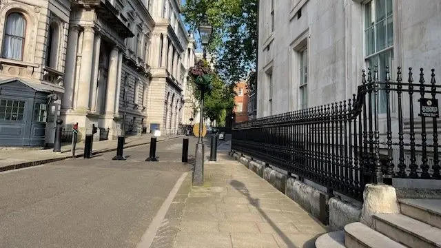 A view of Downing Street on a bright morning. There are steps immediately to the right of where the photo is taken, with bollards halfway up the street