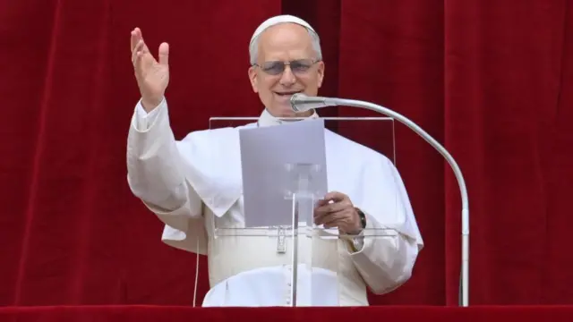 Pope Leo gestures as he speaks into a microphone from a balcony
