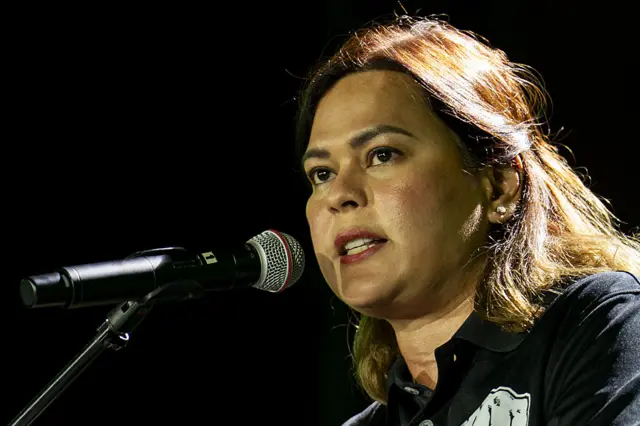 Sara Duterte addressing a crowd through a microphone, while wearing a black T-shirt