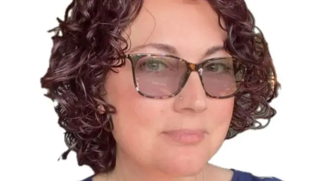 Headshot of Kristy looking at the camera wearing dark framed tinted glasses