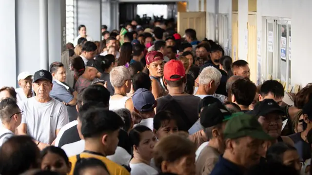 A corridor is packed full of voters, dressed in different colours and looking around in different directions.