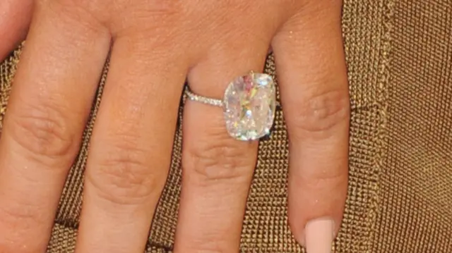 A close up shot of a hand with a large round diamond ring on it