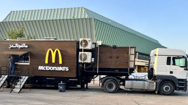 A truck with a McDonald's truck attached to the back, which has the company's logo and a hatch to serve food out of the side