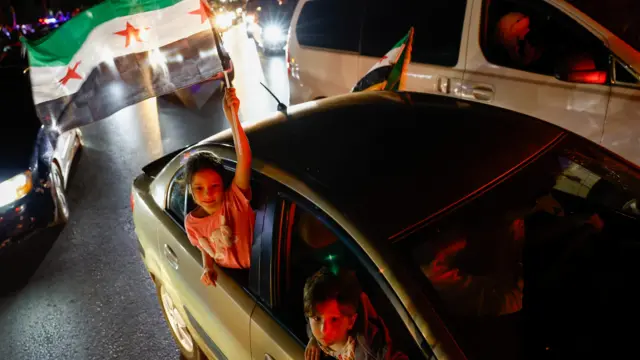 A girl holds a Syrian flag in a moving car