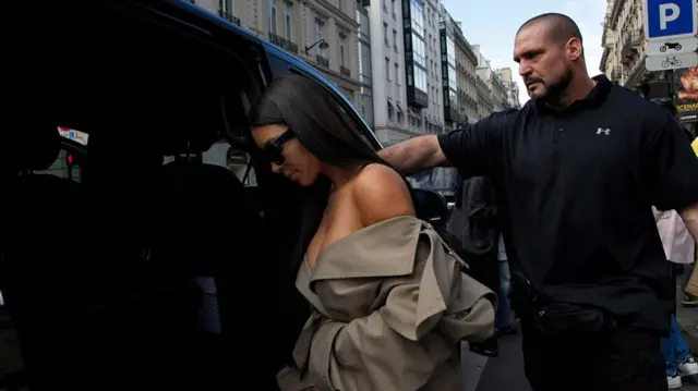 Kardashian getting into a van with a large man holding the door behind her