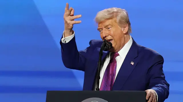Trump holds his hand up high in a gesture as he speaks from the podium