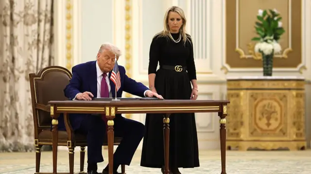 Trump at a large wooden table, ready to sign an agreement.