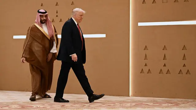 President Trump walking alongside Saudi Crown Prince Mohammed Bin Salman in front of a sandy coloured wall with triangular markings.