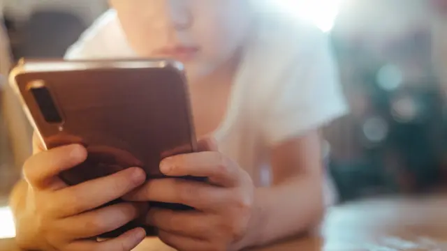 A child lying on the floor holding a mobile phone