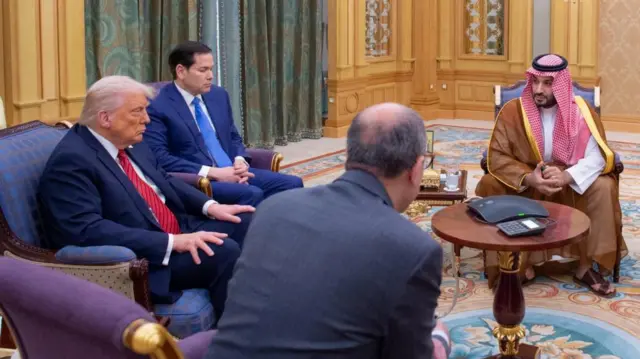 President Trump sits in an armchair looking forwards with his hands on his knees. The Crown Prince sits with his hands clasped, looking at President Trump.