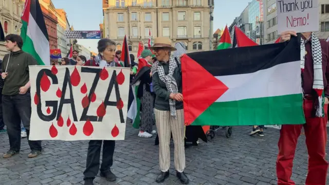 A protestor holds a sign reading 'Gaza', another protestor holds a Palestinian flag