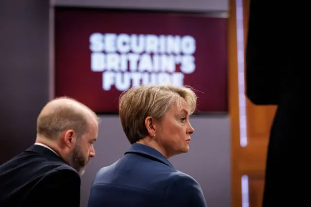 The back of Yvette Cooper sat in front of a sign which says 'Securing Britain's Future' in a Downing Street briefing room