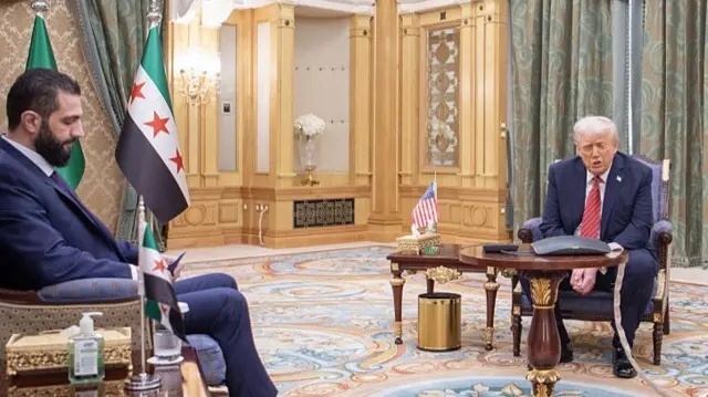 Al-Sharaa sitting looking down as Trump looks opposite him in a fancy room