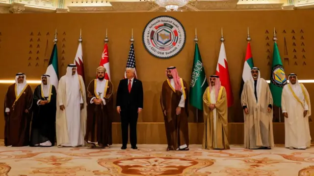 Trump standing alongside other men looking to the side in front of flags