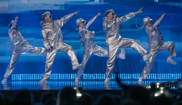 A group of people in silver suits dance