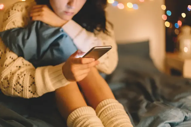 A girl on a mobile phone with her hands hugging her knees