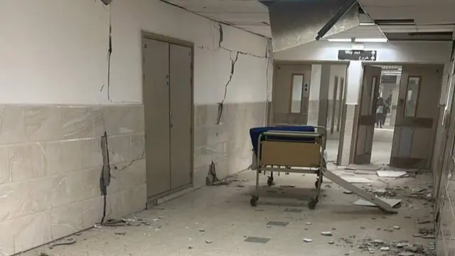 Debris on the floor of the European hospital in Gaza. There are cracks on the walls and a discarded bed sits in the middle of the corridor.