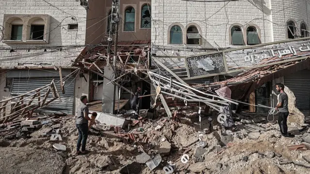 People walk outside rubble in front of a hospital with part of the front of the building fallen down from a bomb