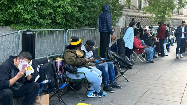 People sit and wait in line on folding chairs