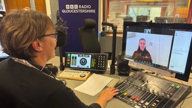 Nicky speaks to Maddy on Zoom. Nicky is sitting at a desk in a radio studio, with lots of equipment around her.