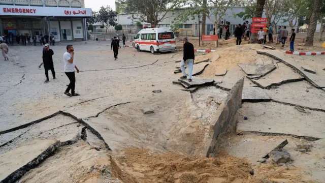 People walk around a crater caused by bombs outside a hospital in Gaza