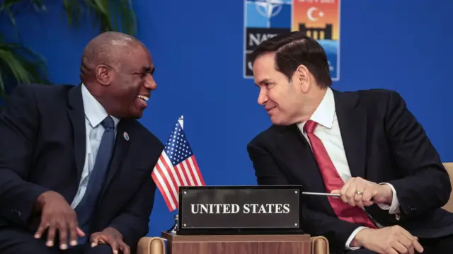 Rubio and David Lammy are seated and smile at one another across a table with a sign reading 'United States'