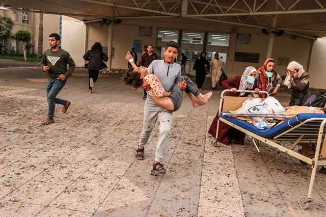 A young man carries a child wearing a hospital band in his arms as he runs away from a hospital that was hit by a strike