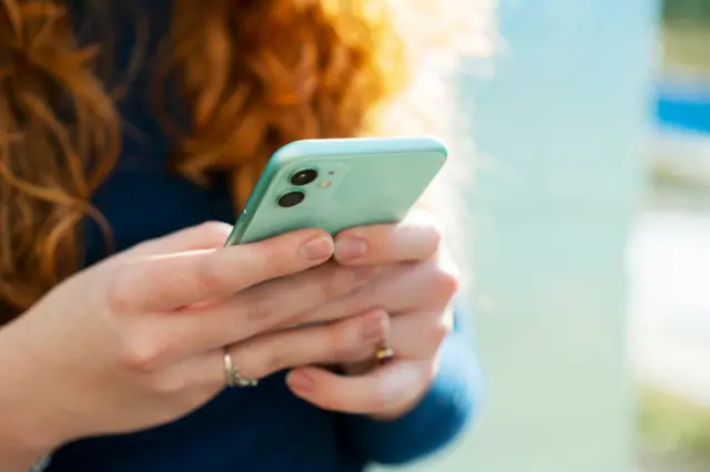 A woman with long red hair holds a blue smartphone.