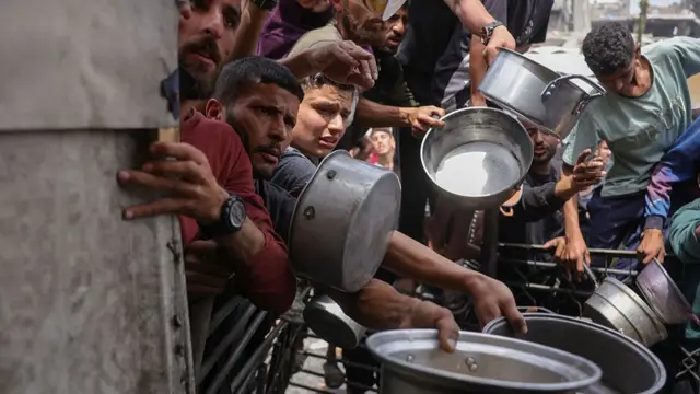 Men hold out large steel pans for food at a distribution centre in Gaza