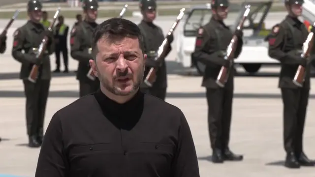 Zelensky speaks on the tarmac at airport in front of military guards and aircraft
