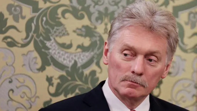 Dmitry Peskov stood in front of floral wallpaper.