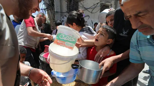 A boy and other Palestinians hold out bowls and pans for food from aid workers
