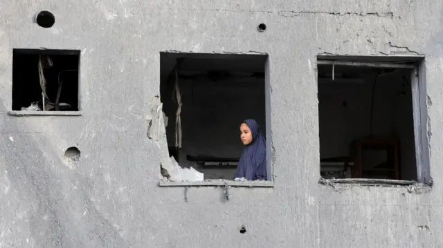 A young woman looks out of a glass-less window of a severely damaged concrete building