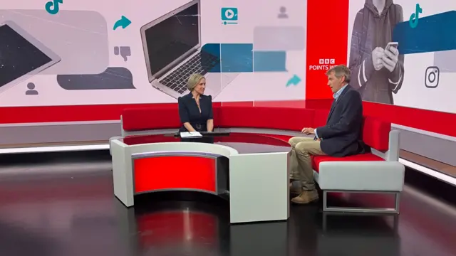 A man and a woman speaking on a red sofa inside a large, digital TV set for news programmes