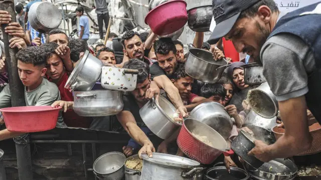 People hold bowls out for food in a queue