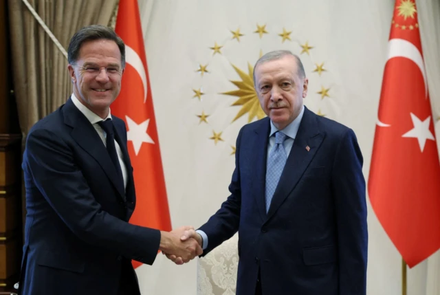 Turkey's President Tayyip Erdogan meets with Nato Secretary General Mark Rutte pose shaking hands in front of two Turkish red flags
