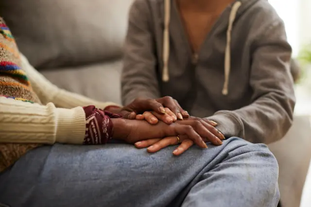 A stock image of two women holding hands as they talk.