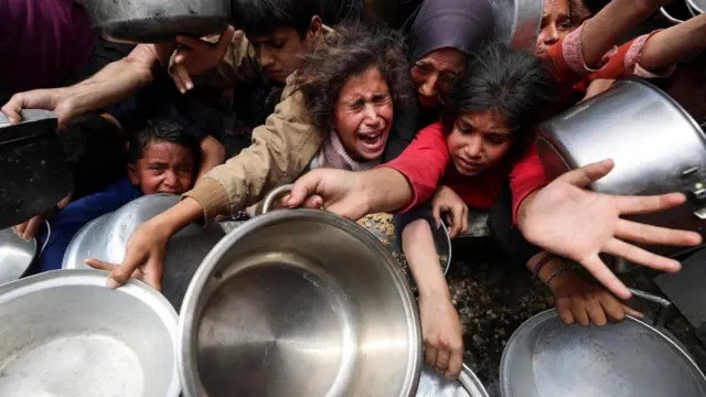 Palestinians wait to receive food cooked by a charity kitchen, in Jabalia, in the northern Gaza Strip