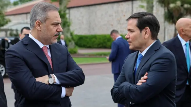 Rubio facing Turkish foreign minister both with arms folded in conversation.