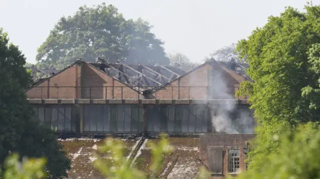 charred warehouse that is smoking is shown among trees